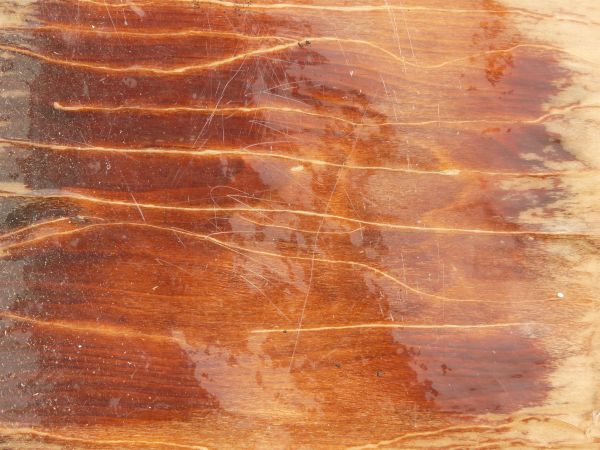 Laquered wood texture, with a scratched, glossy surface covering the reddish brown board.
